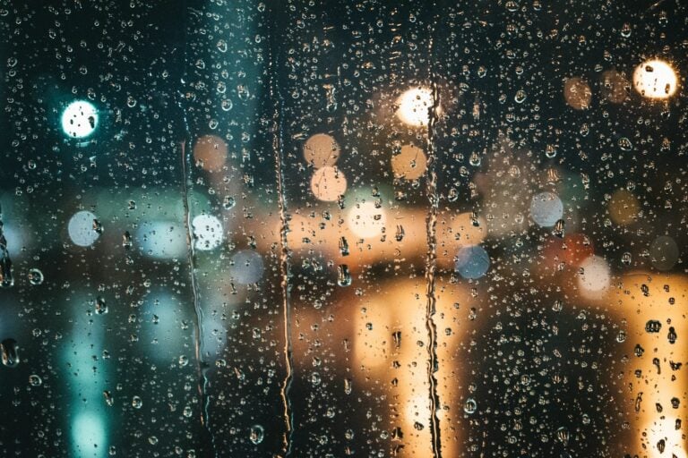 Rain on a window at night with warm lights beyond