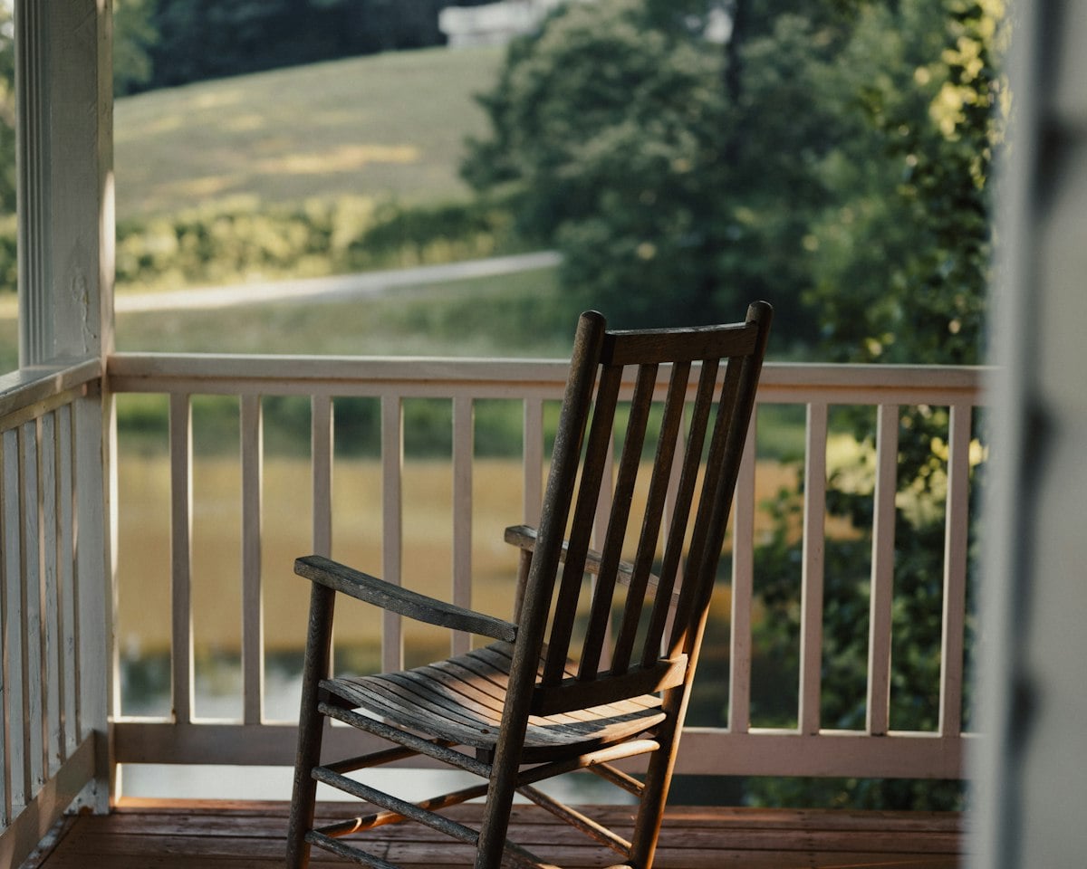 A rocking chair on a sunlit front porch, looking out over green pastures